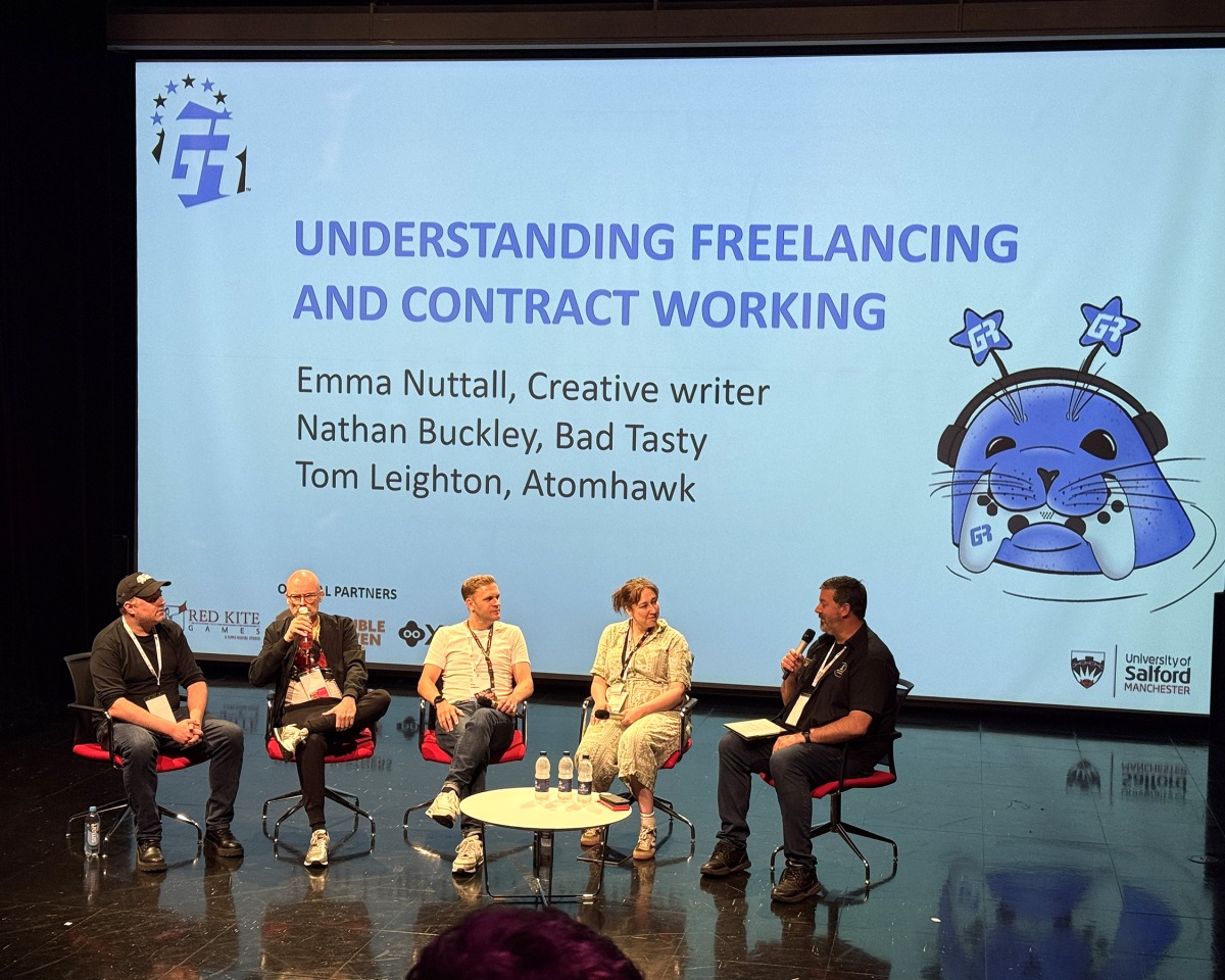 Five panellists sit on stage beneath a screen displaying “Understanding Freelancing and Contract Working,” with names and roles listed. Event logos, a cartoon cat with headphones, and the Atomhawk logo are shown on the screen, emphasising the future of visual development in creative industries.